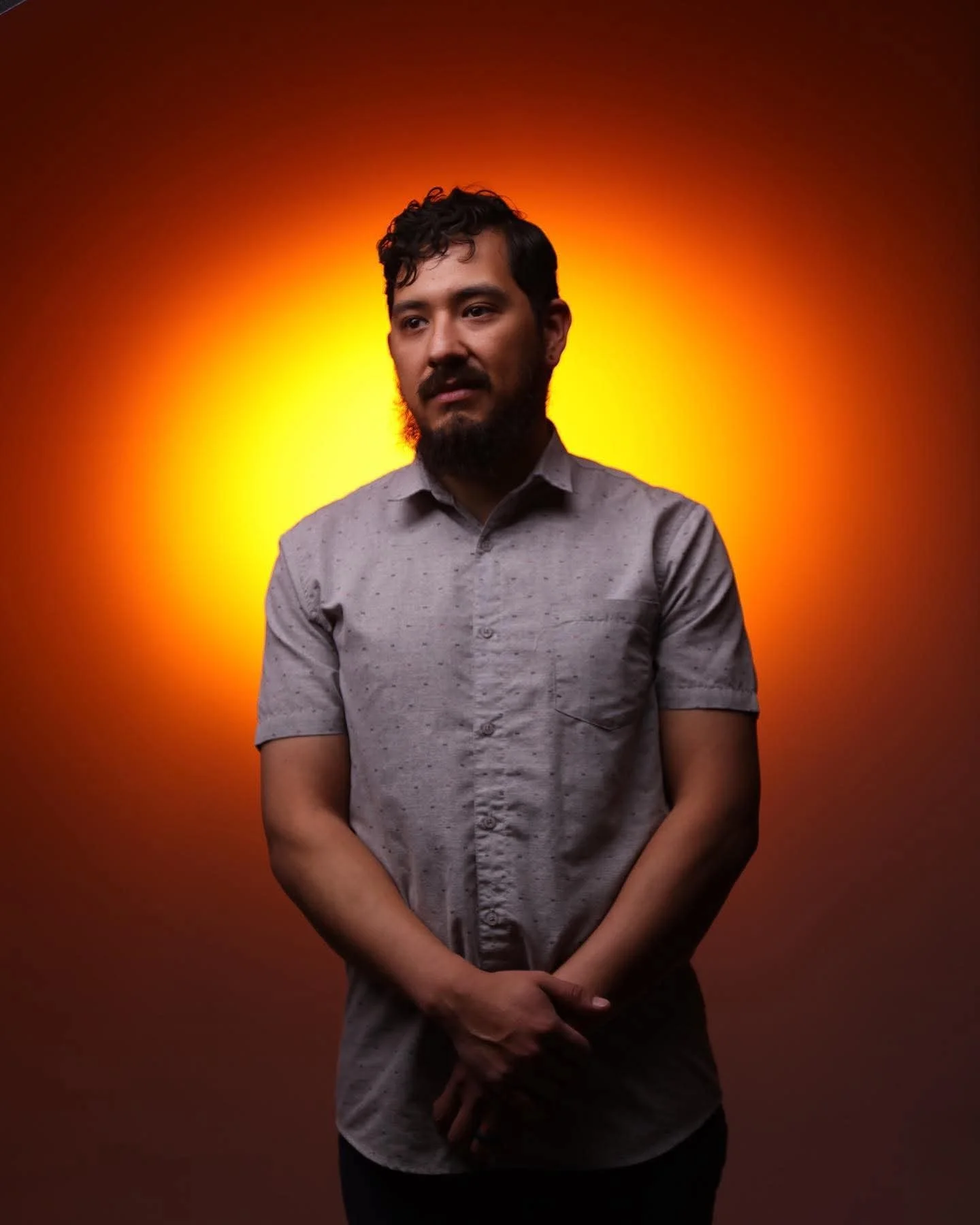 A portrait of Harvey Garza, founder of HG Productions, in a short-sleeved button-down shirt against a vibrant orange and yellow studio background in Lubbock Texas