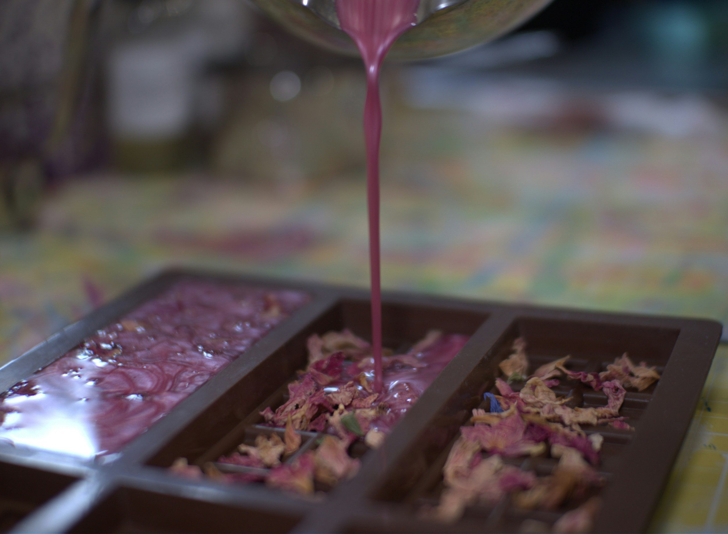 Close-up of a chocolate mold filled with pink-colored chocolate pouring into the mold from above.