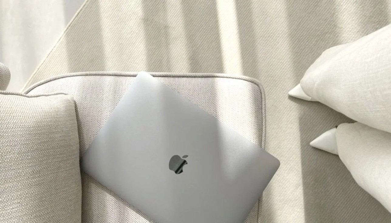 Top view of a MacBook placed on a light-colored sofa, with white cushions nearby.