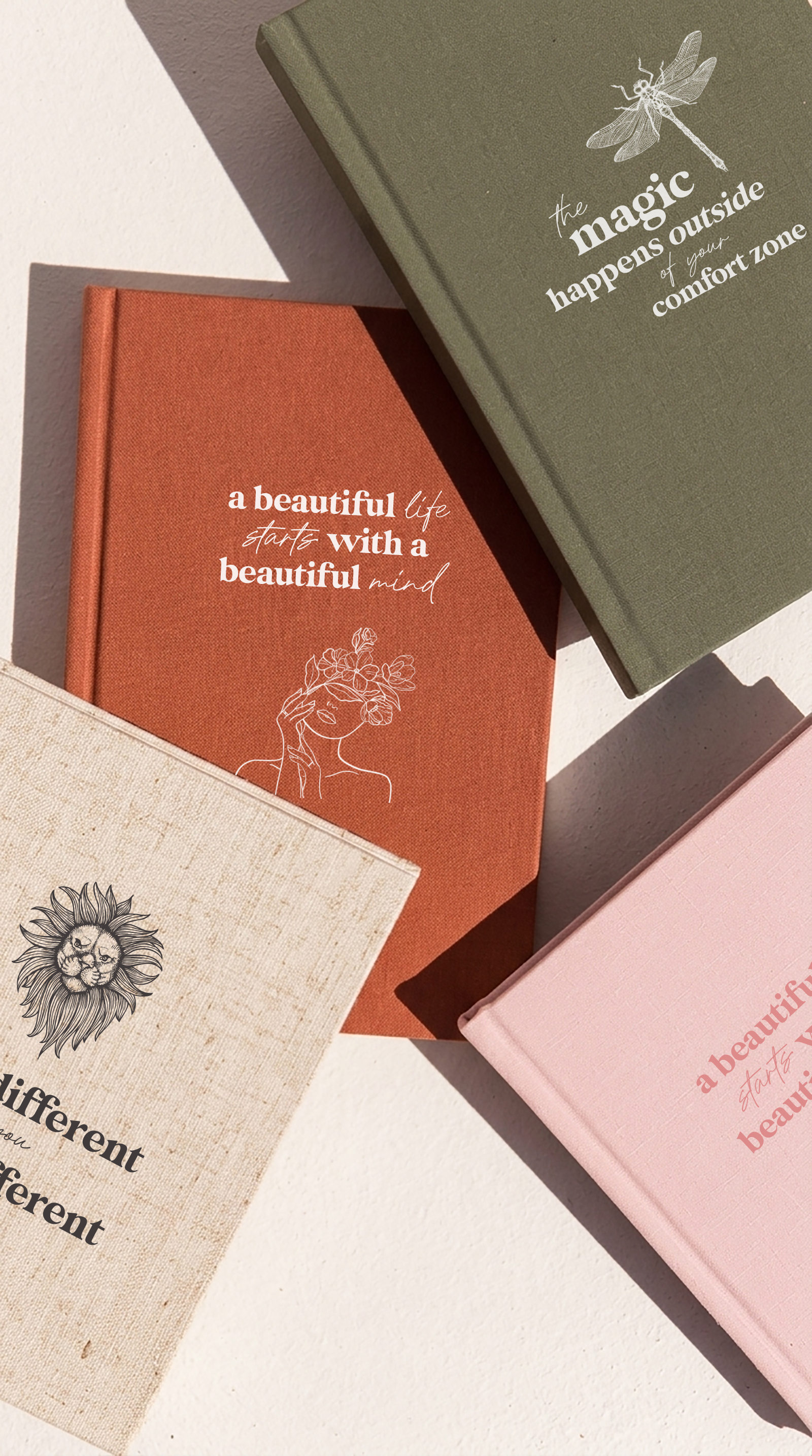 Several closed books with motivational quotes and illustrations on their covers, arranged on a white surface with shadows cast by sunlight.