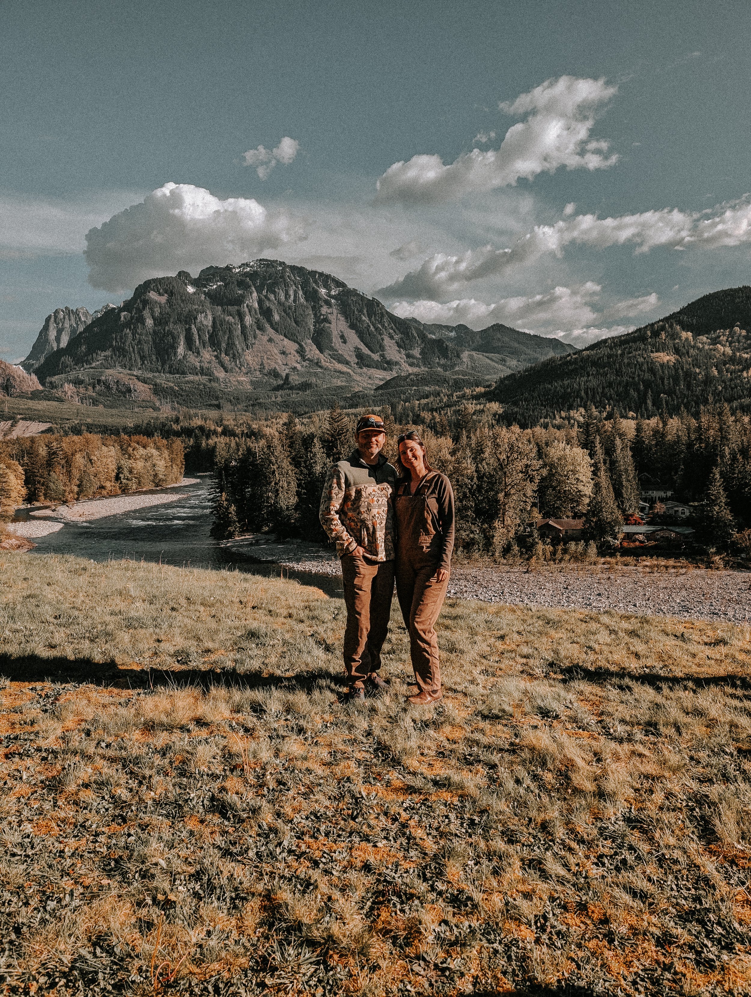 A photo of Field & Fern founder, Jill, with her partner, Matt, standing together in front of a mountain and river landscape.