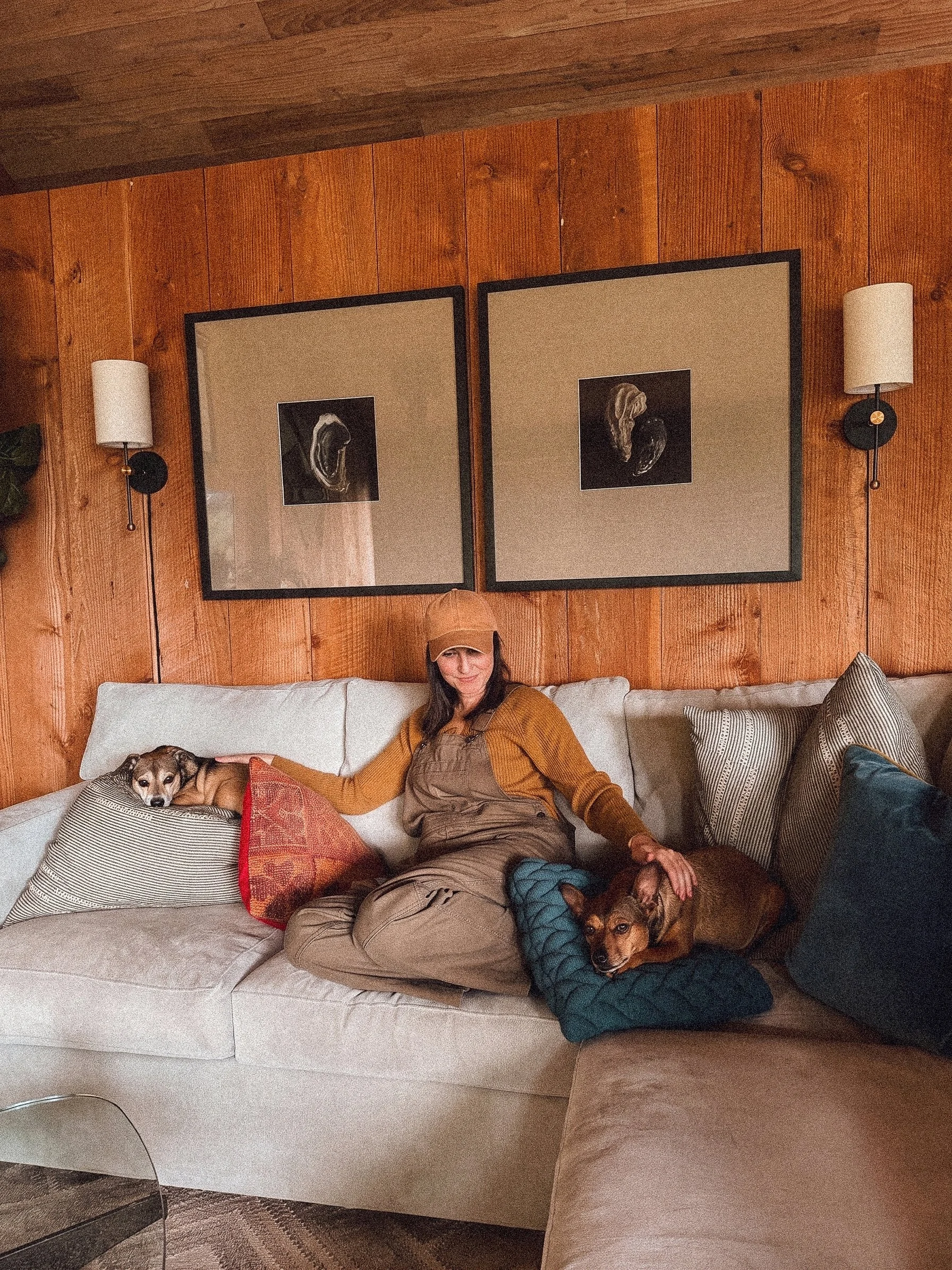 A woman sitting on a warm sofa with two dogs, in a PNW cabin.
