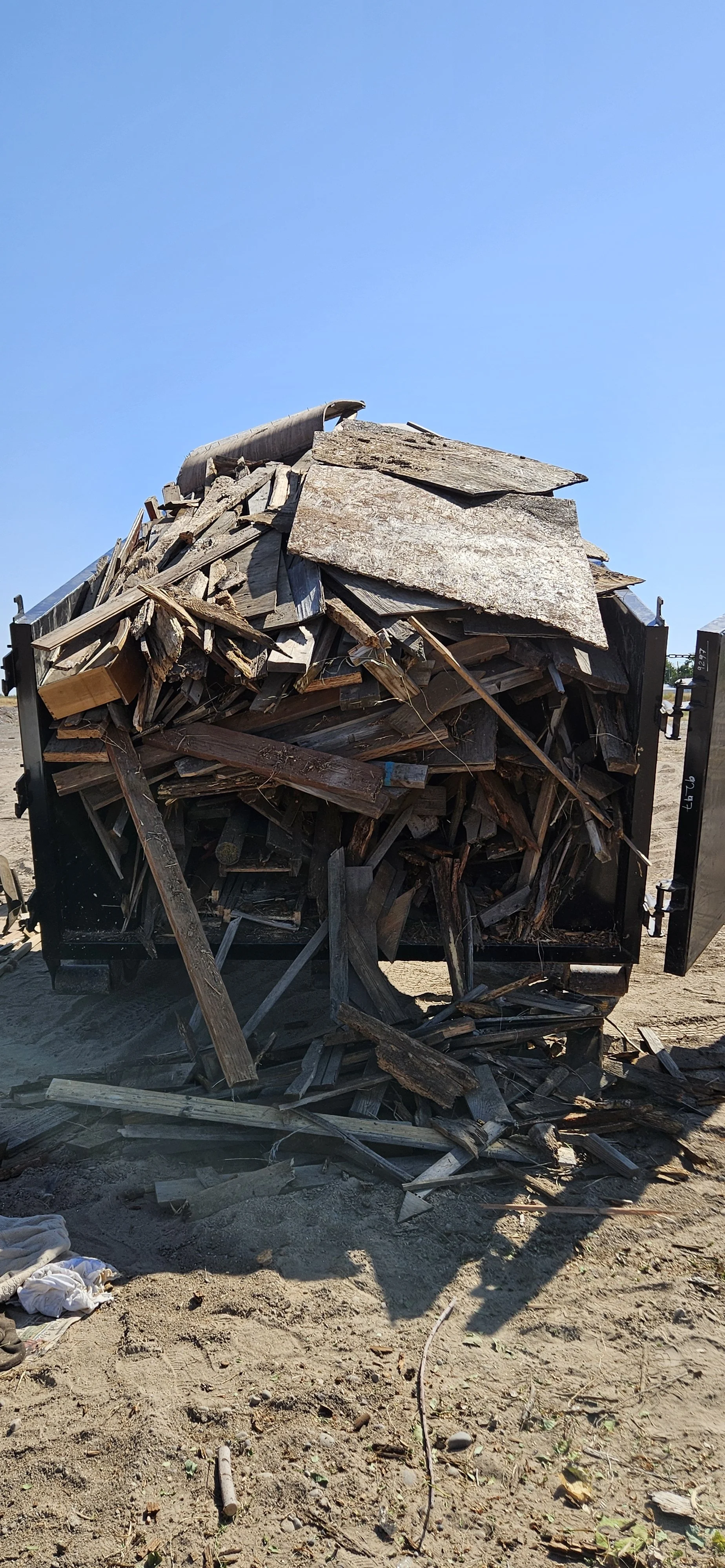 Pile of discarded wood and debris in an outdoor setting under a clear blue sky.
