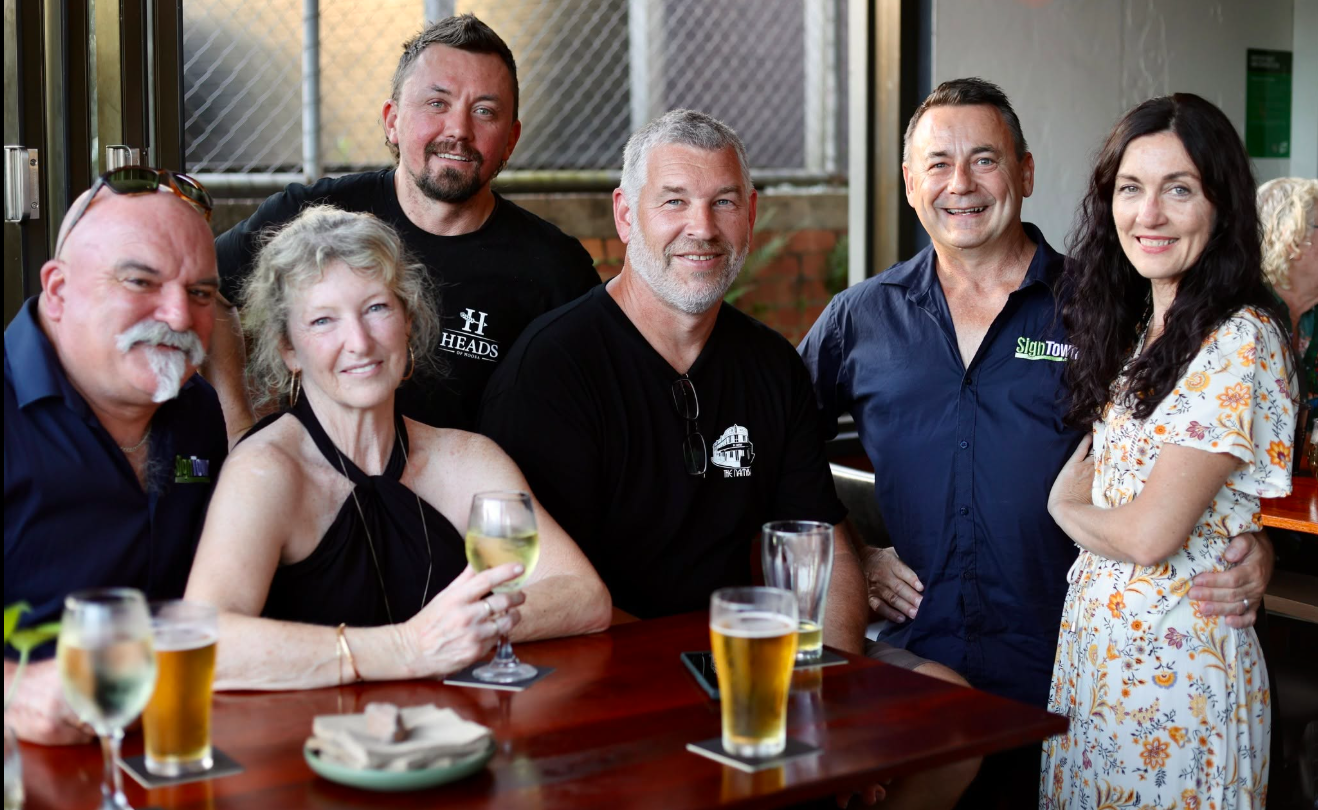 Group of six adults smiling at a table with drinks, indoors at a social gathering.