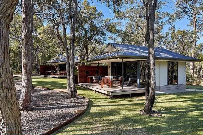 A modern house with a metal roof and large front porch, surrounded by trees and a grassy yard.
