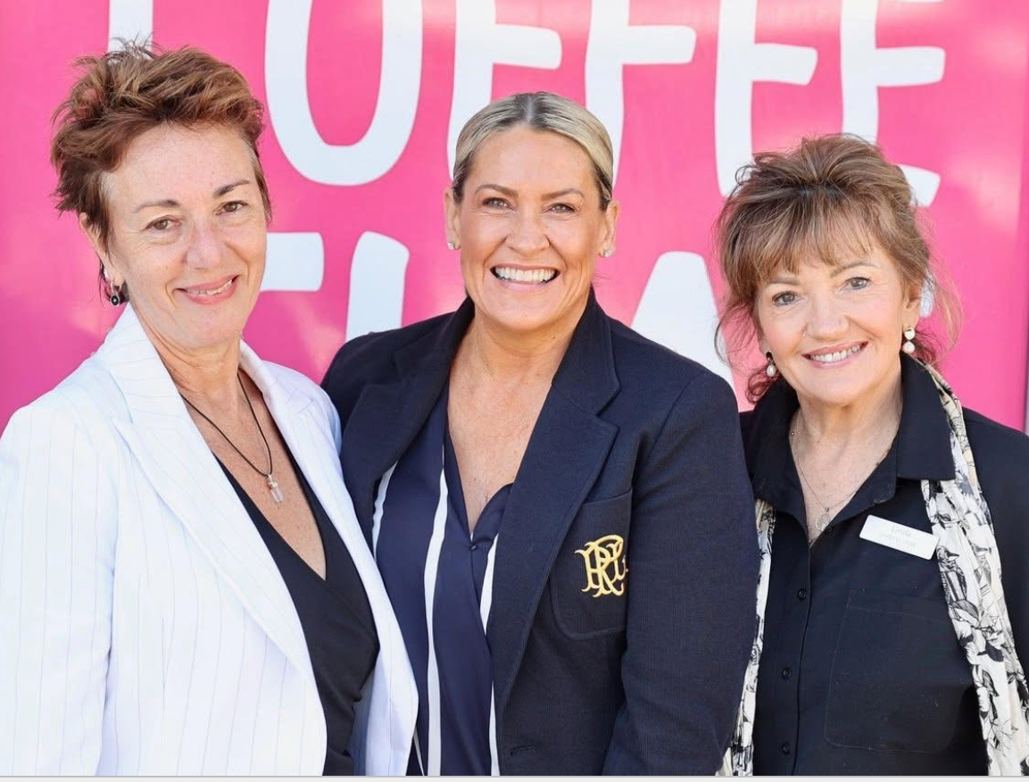 Three women smiling in front of a pink background with large white lettering.