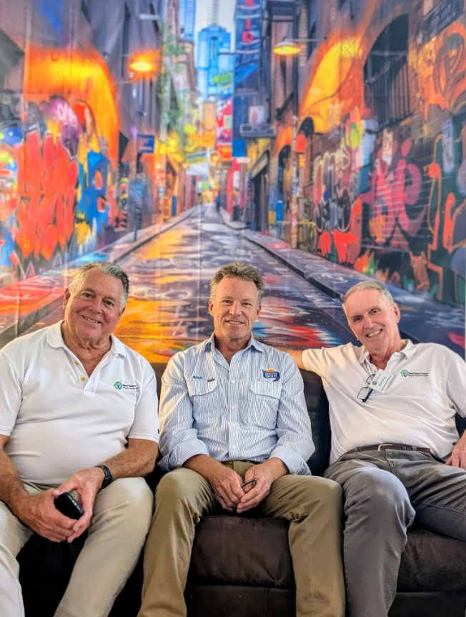 Three men sitting on a sofa in front of a colorful graffiti wall.