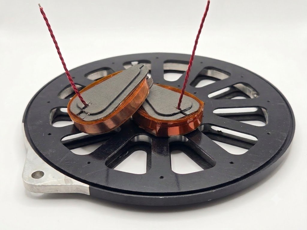 A speaker coil placed on a speaker frame with red suspension wires.