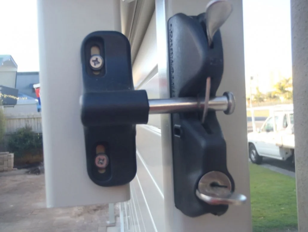Close-up of a door latch with a keyhole in a white door, with a background of a driveway, grass, and parked cars.