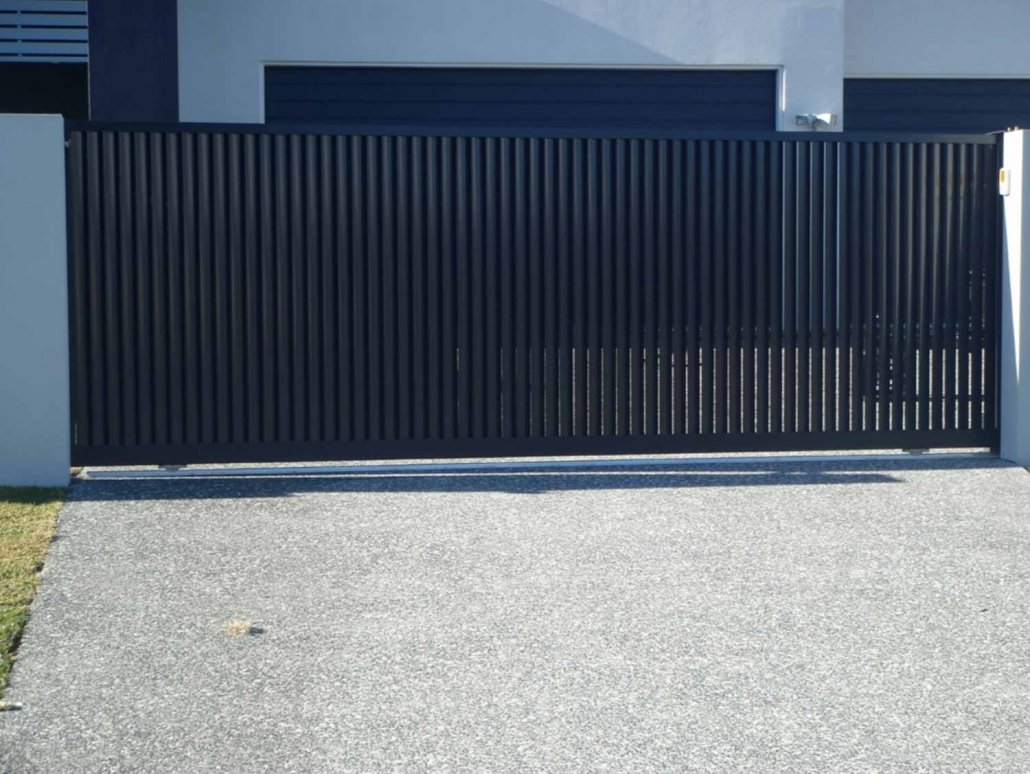 Black sliding gate in front of a modern house with a concrete driveway.