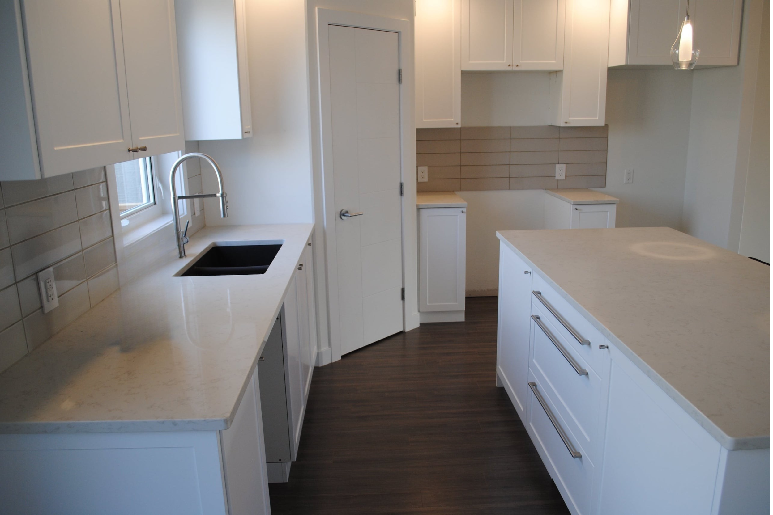 Modern kitchen with white cabinets, marble countertops, a black sink, a window above the sink, a tiled backsplash, and dark wood flooring.