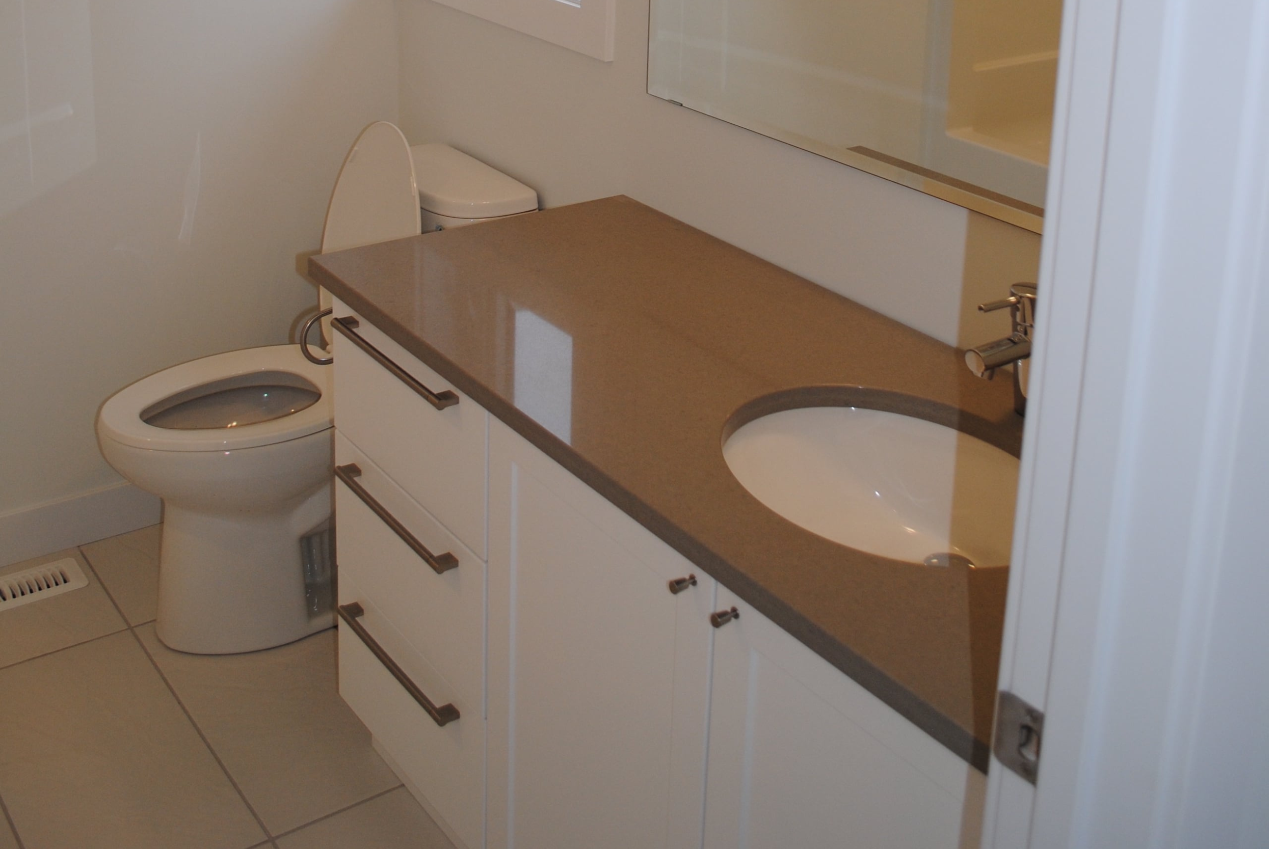 A bathroom featuring a toilet, a brown countertop with a sink, a mirror, and white cabinet drawers.