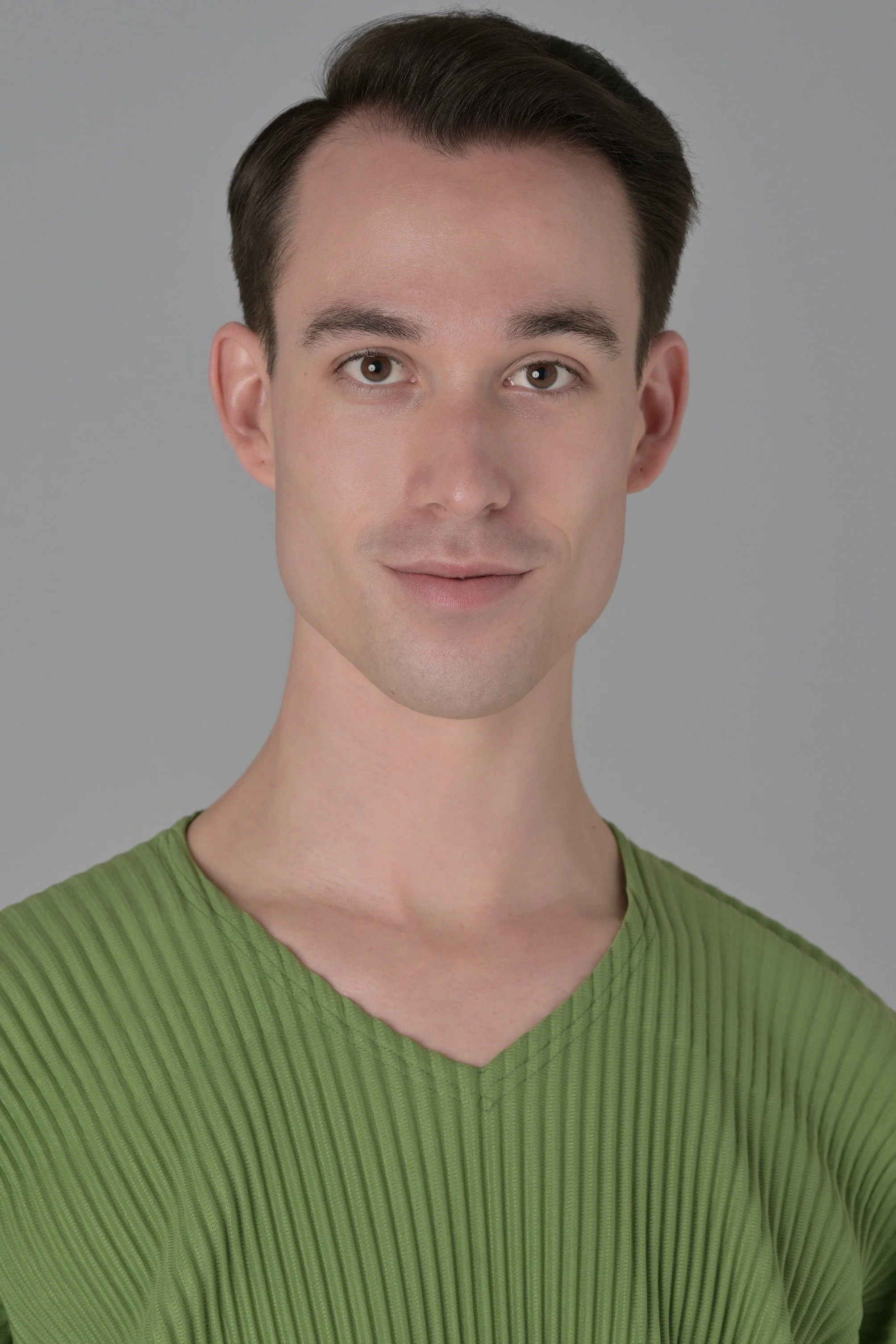 Close-up of a young man with brown hair, light skin, and brown eyes, wearing a green ribbed shirt, smiling softly against a plain gray background.