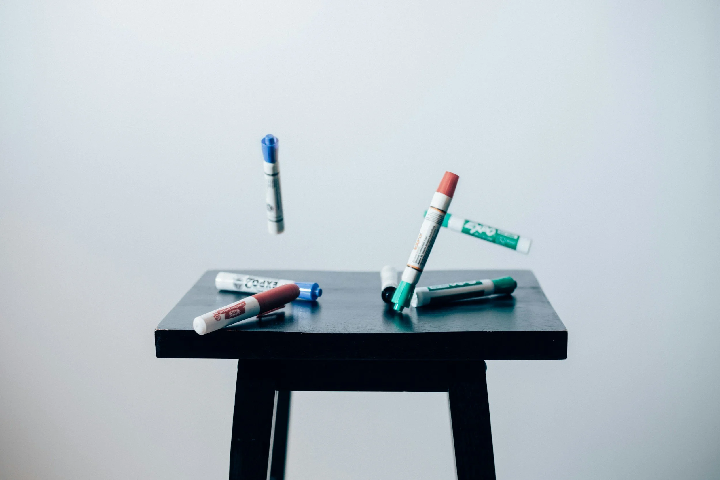 Markers scattered on a black table with a plain gray background.