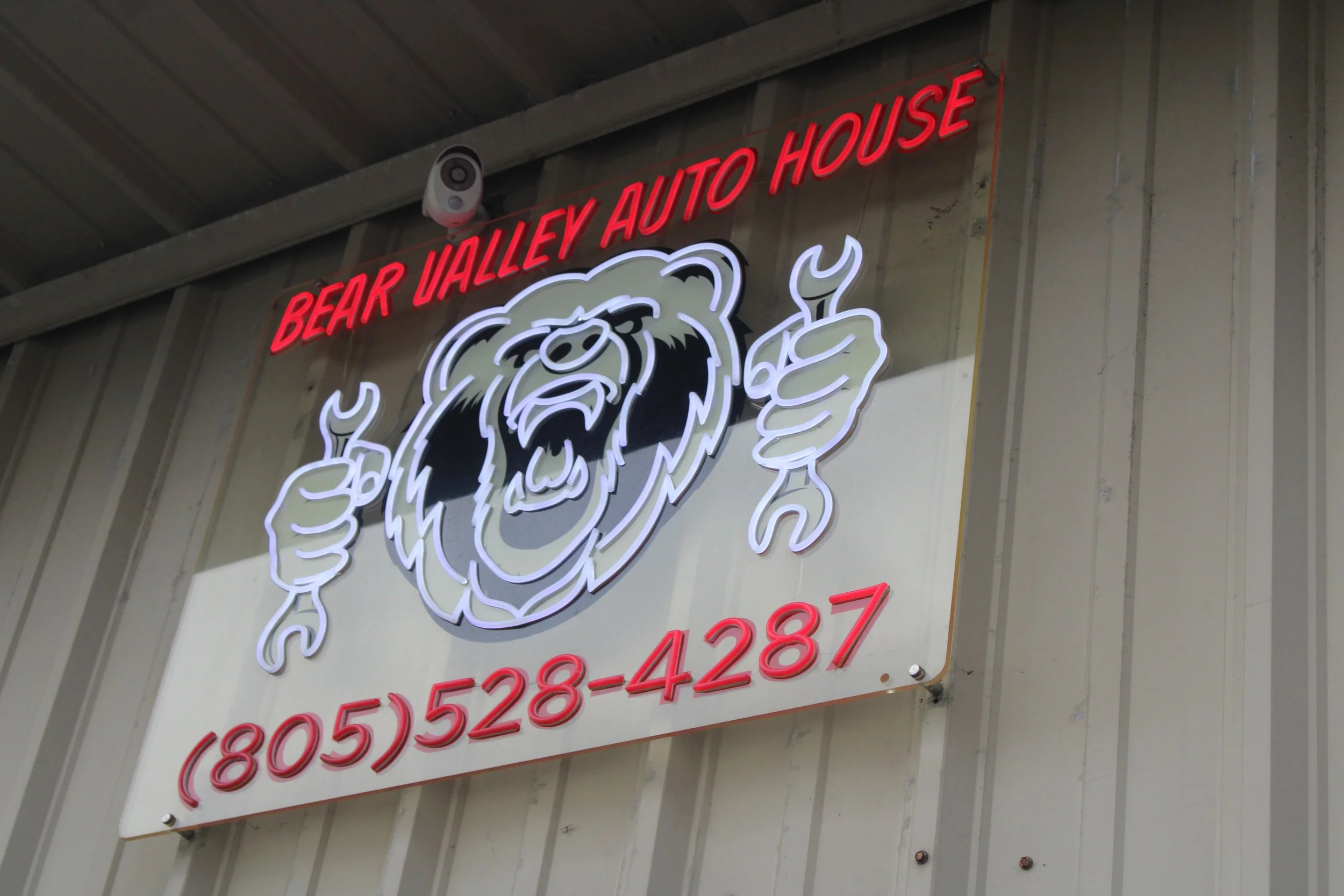 Neon sign for Bear Valley Auto House featuring a bear with two thumbs up, and phone number below.