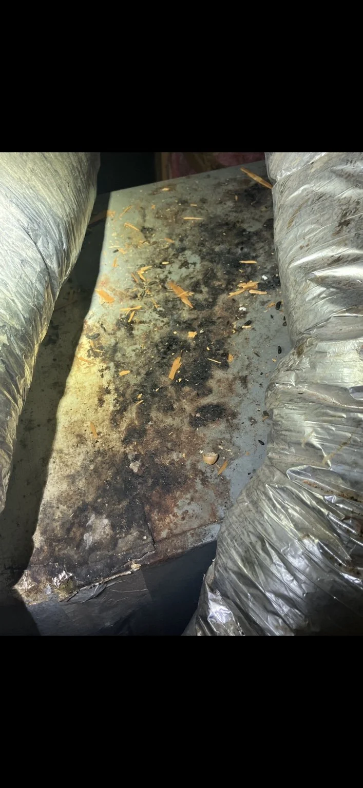A grimy work table with black and brown stains and scattered wood shavings, flanked by duct hoses on either side.