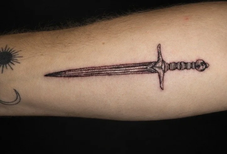 Tattoo of a sword on a person's forearm.