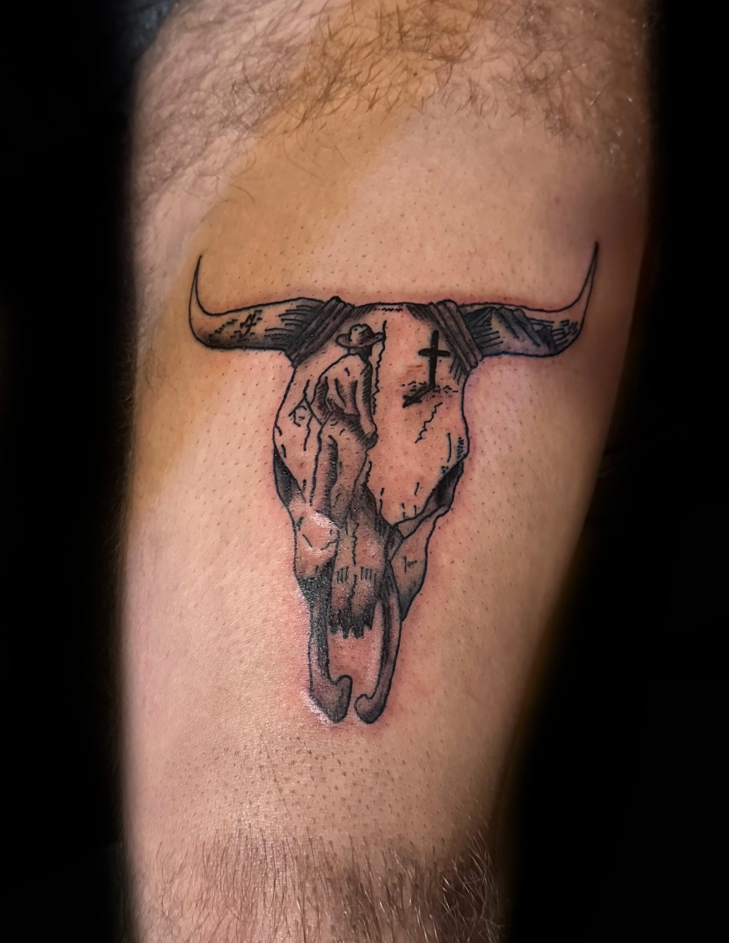 Tattoo of a cow skull with a man inside it looking out over the horizon to a grave on skin.