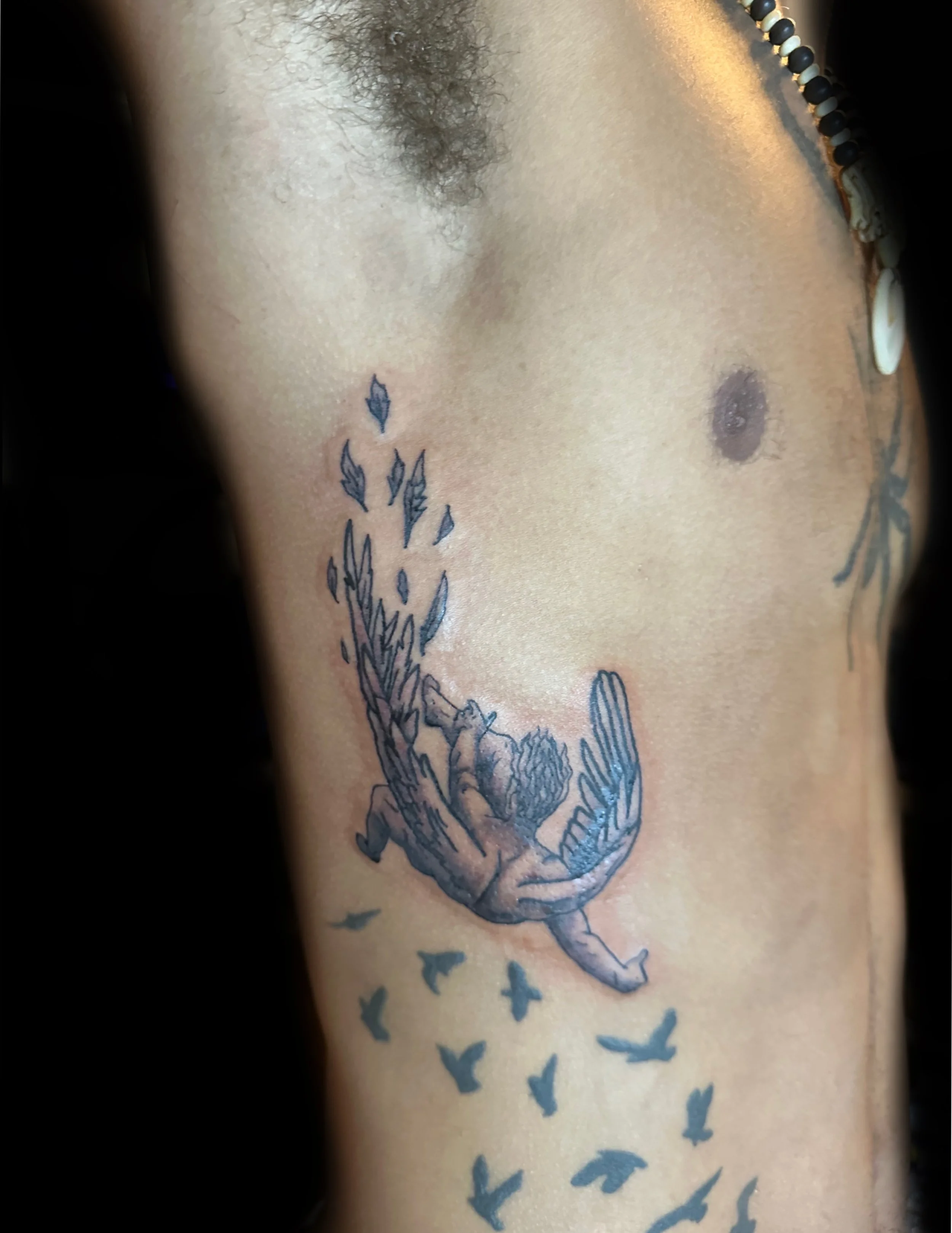 Tattoo of a falling angel with feathers flowing behind him on a person's arm, with birds flying below it.