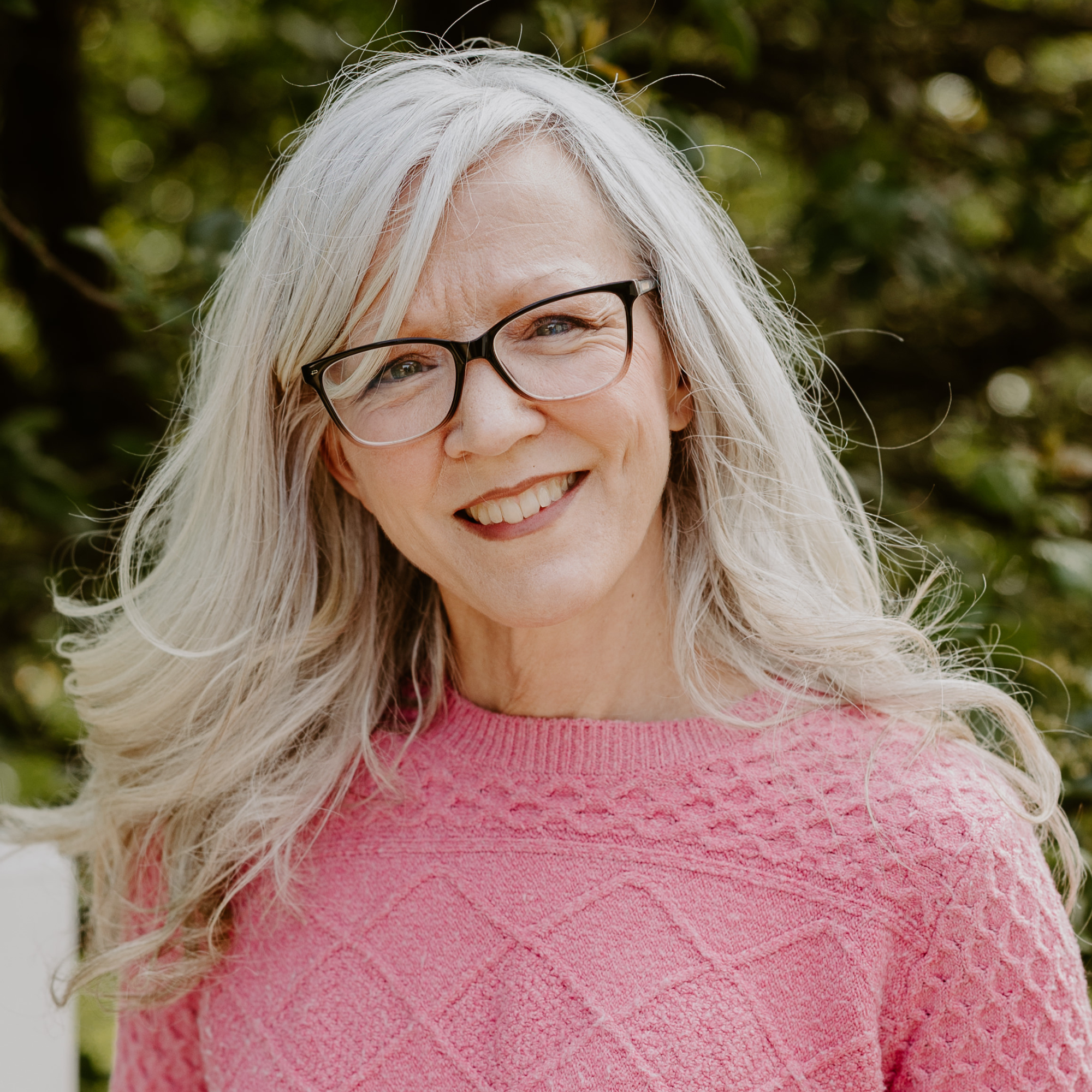 A smiling woman with glasses and styled gray hair outdoors.
