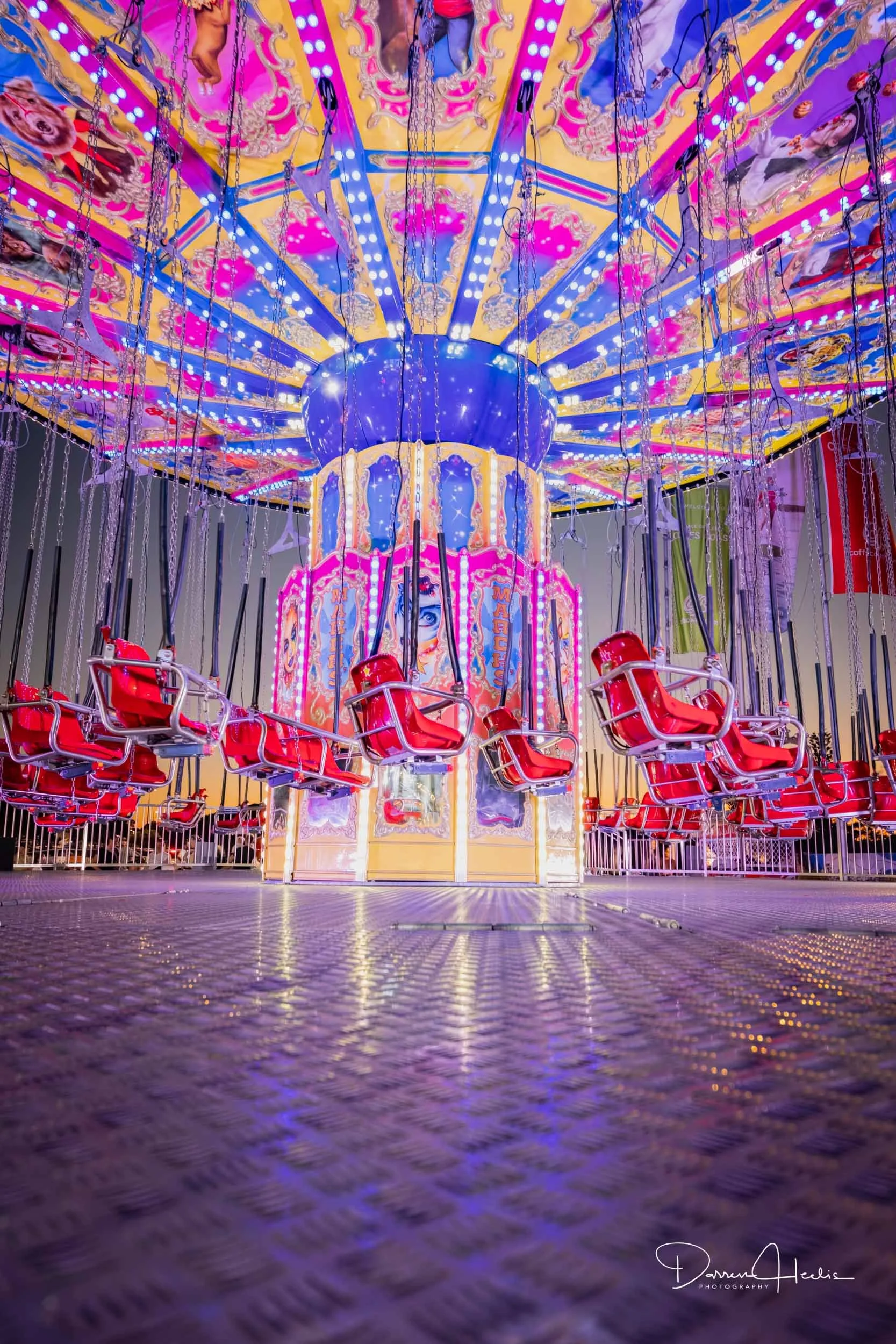 Colorful amusement park ride with red swing seats hanging from chains, decorated with bright lights and pink, yellow, and purple painted panels, illuminated in a vibrant, festive atmosphere.