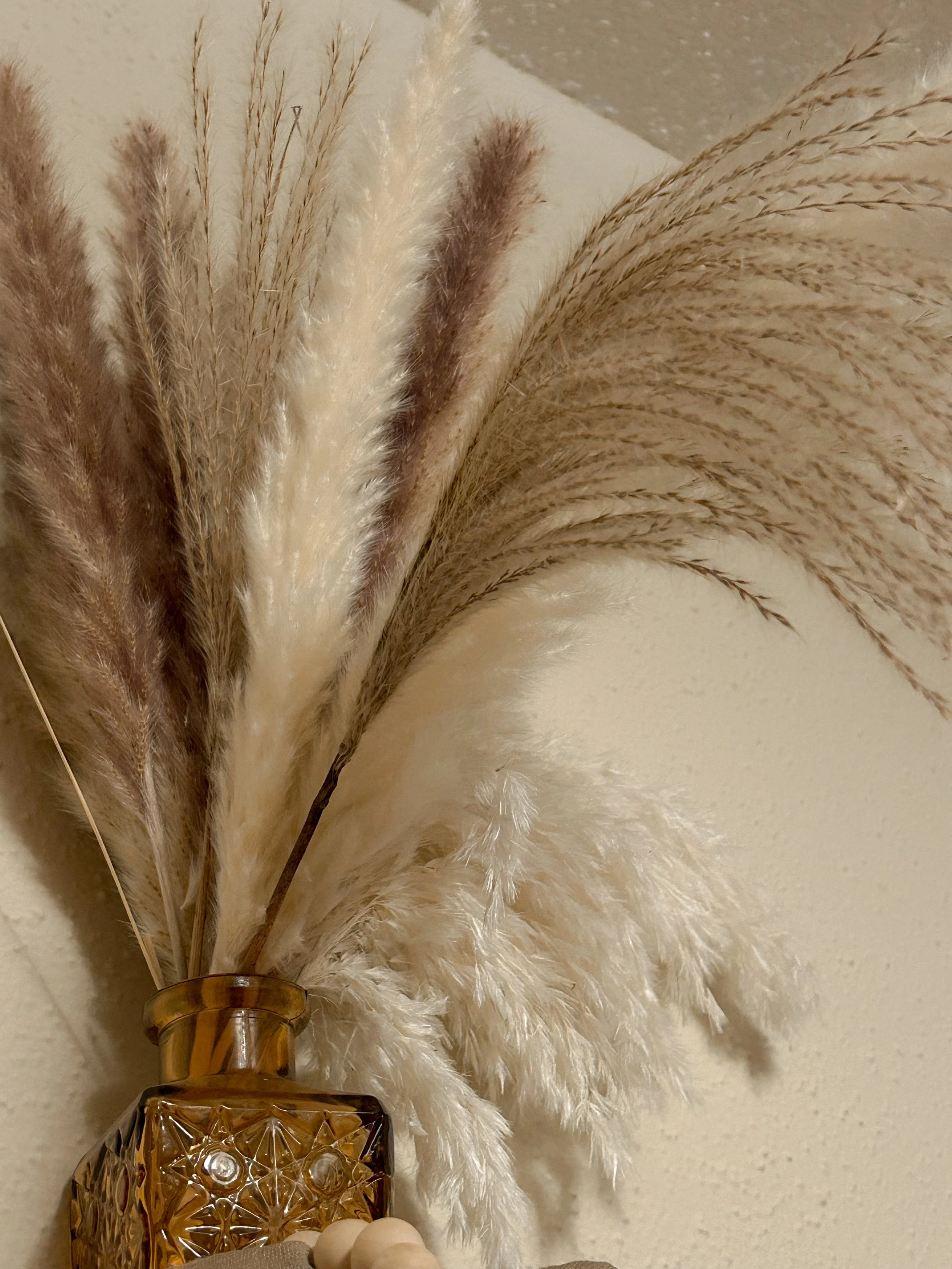 A decorative arrangement with dried beige and brown pampas grass in a crystal amber-colored vase with a textured pattern.