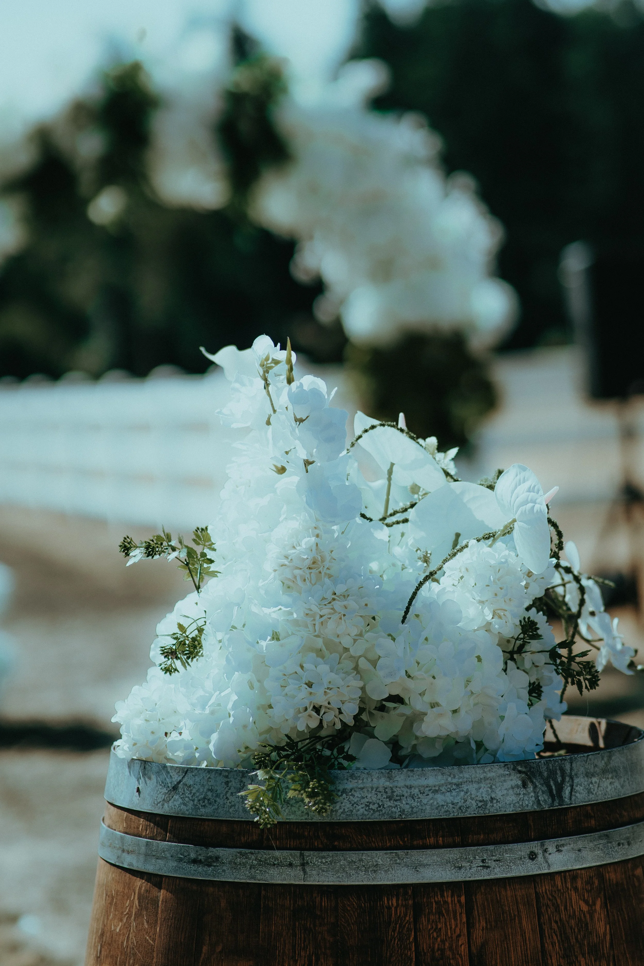 A bouquet of white flowers on a wooden barrel outdoors, with blurred greenery in the background.