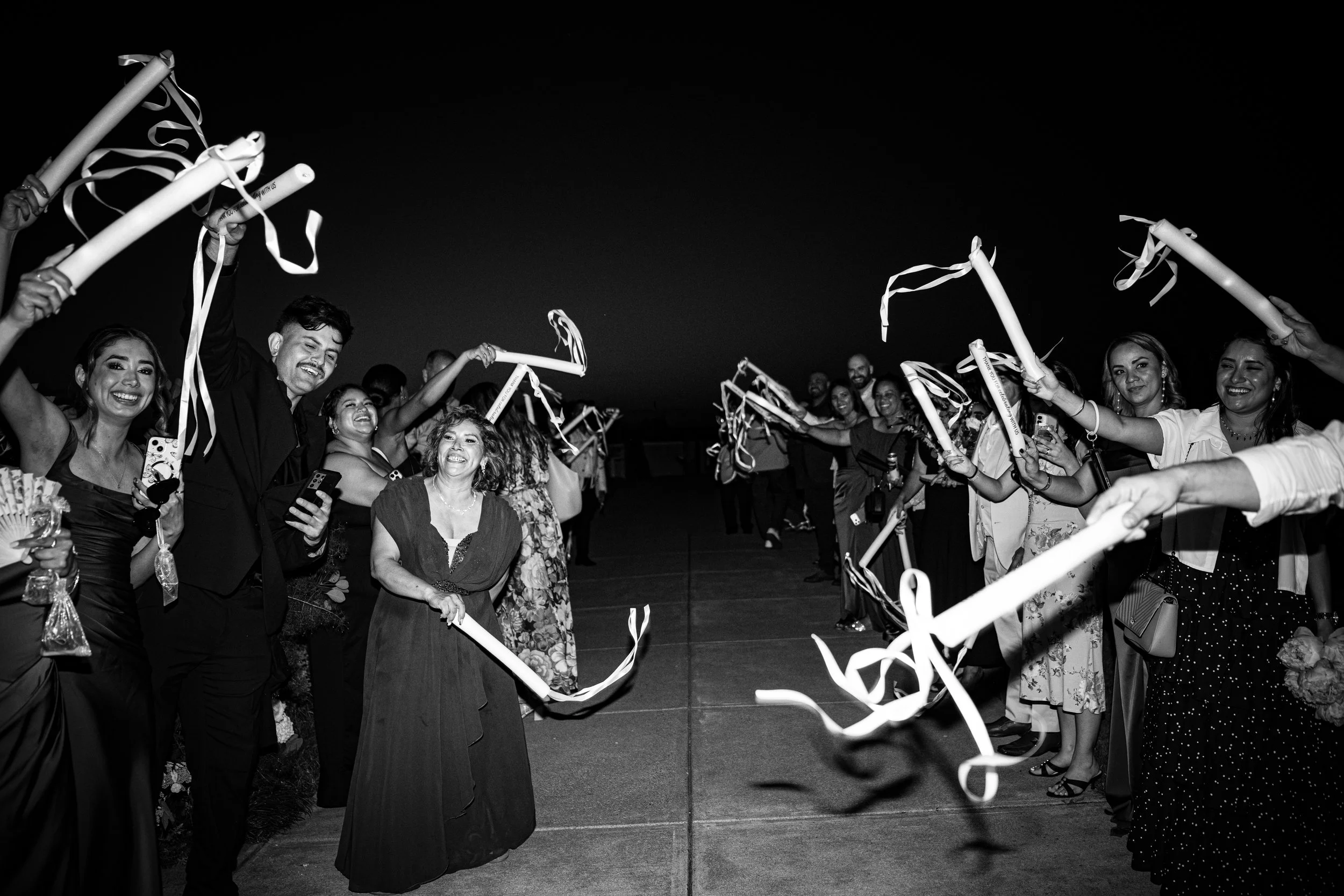 Group of people celebrating outdoors at night, holding paper scrolls and ribbons, with smiling faces.