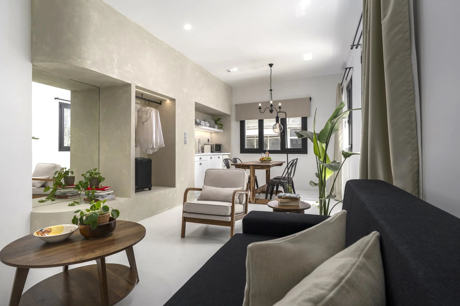 Modern living room with beige and white walls, black and beige furniture, green plants, and large windows with curtains.
