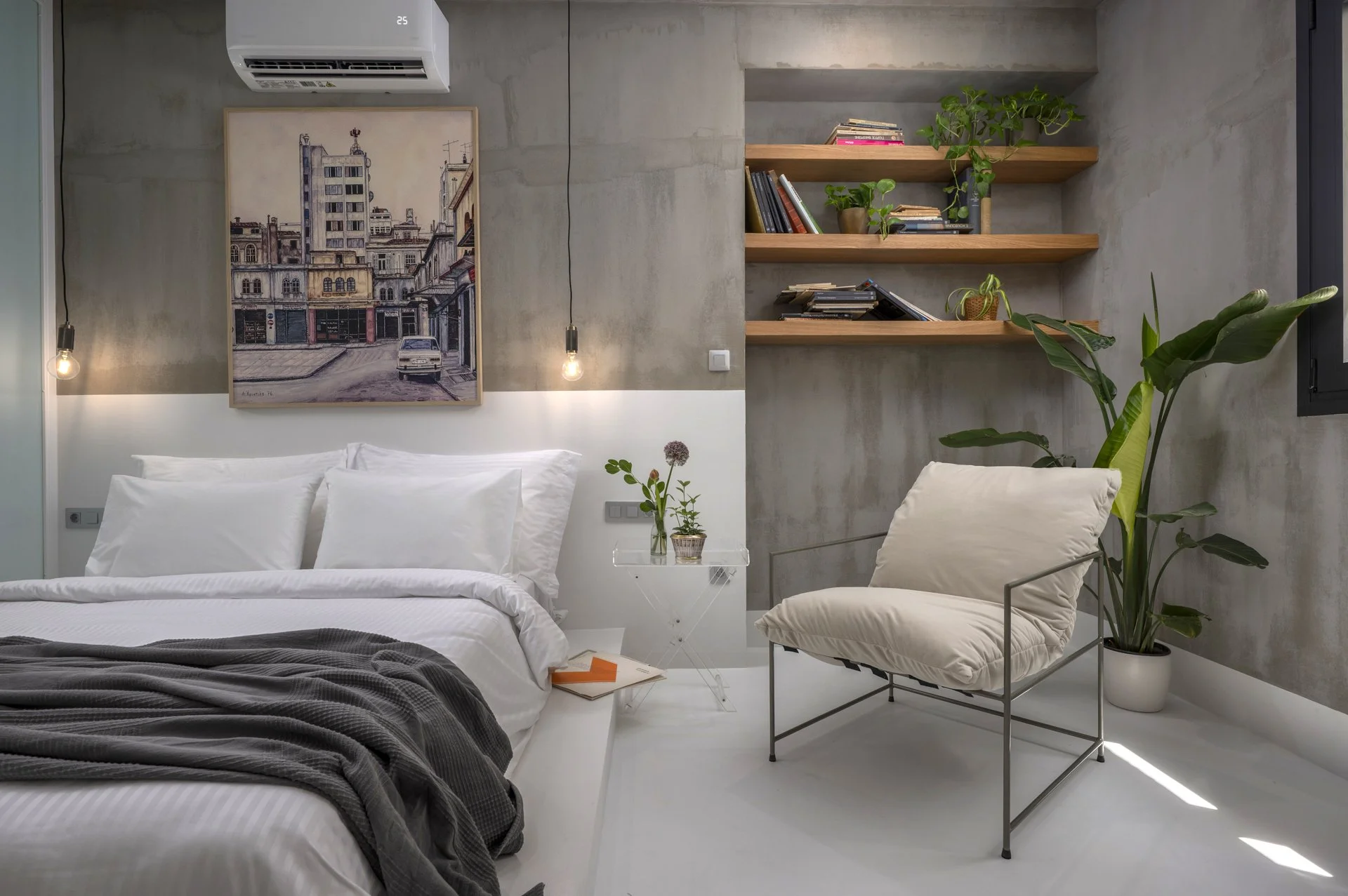 A modern bedroom with a bed, a side table with a flower vase, a white armchair, and built-in wooden shelves with books and plants on a concrete wall. There is an air conditioner unit and a picture of a cityscape on the wall.