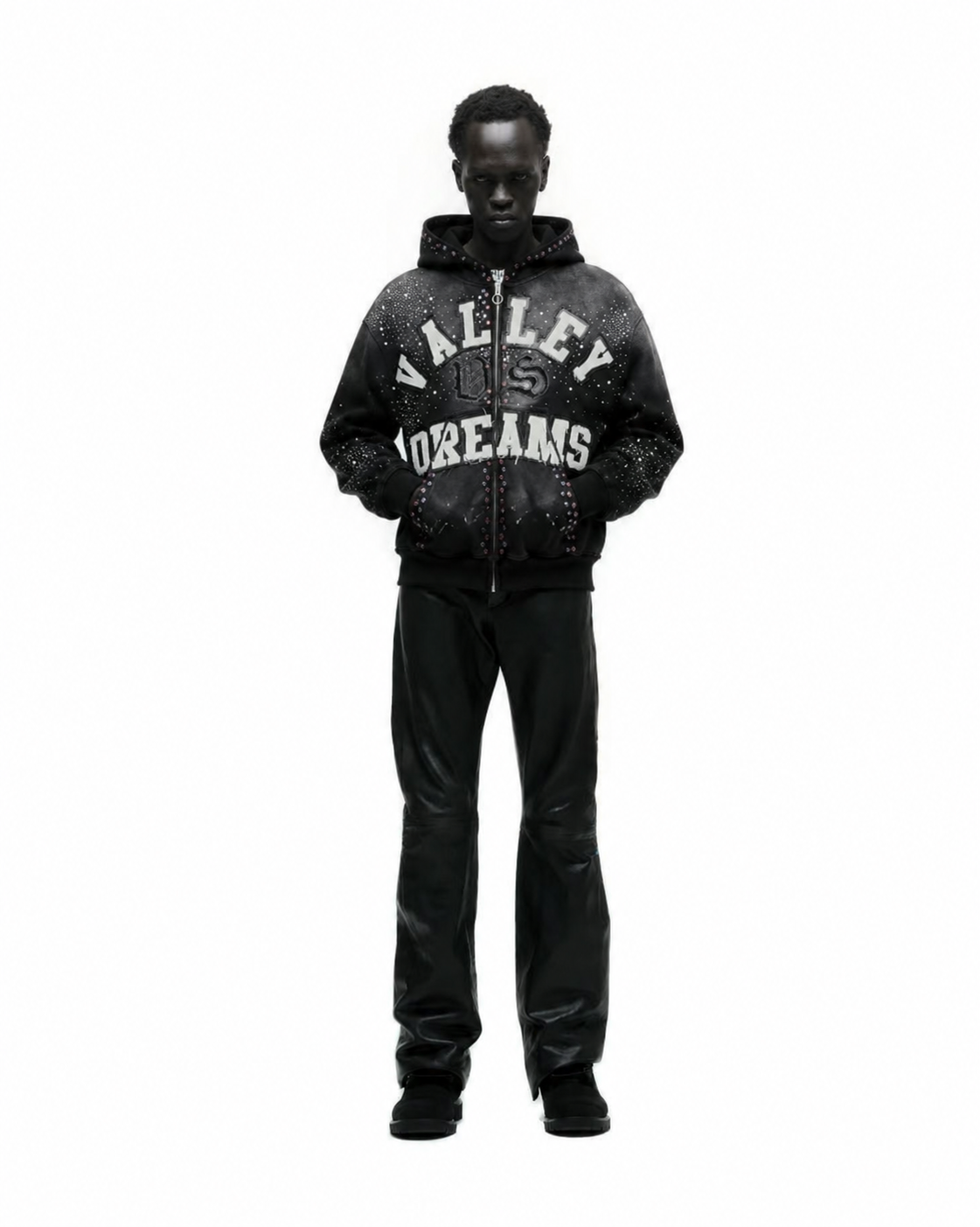 A person with dark skin and short curly hair stands against a plain white background, wearing a black hoodie with 'Vallefy Dreams' written on it, black pants, and black boots.