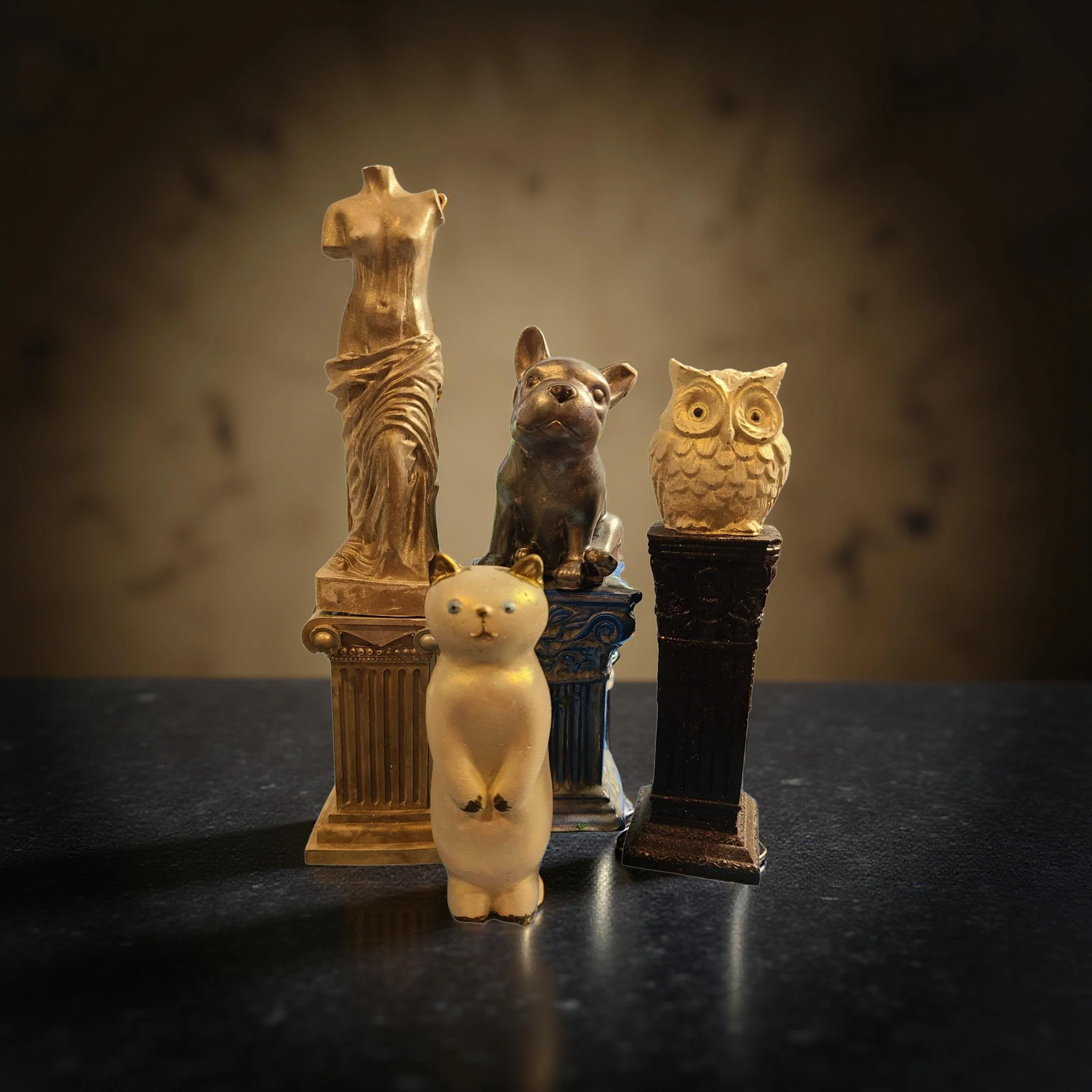 Close-up of small decorative figurines on a dark surface, including a female torso, a dog, an owl, and a rabbit, with a blurred dark background.