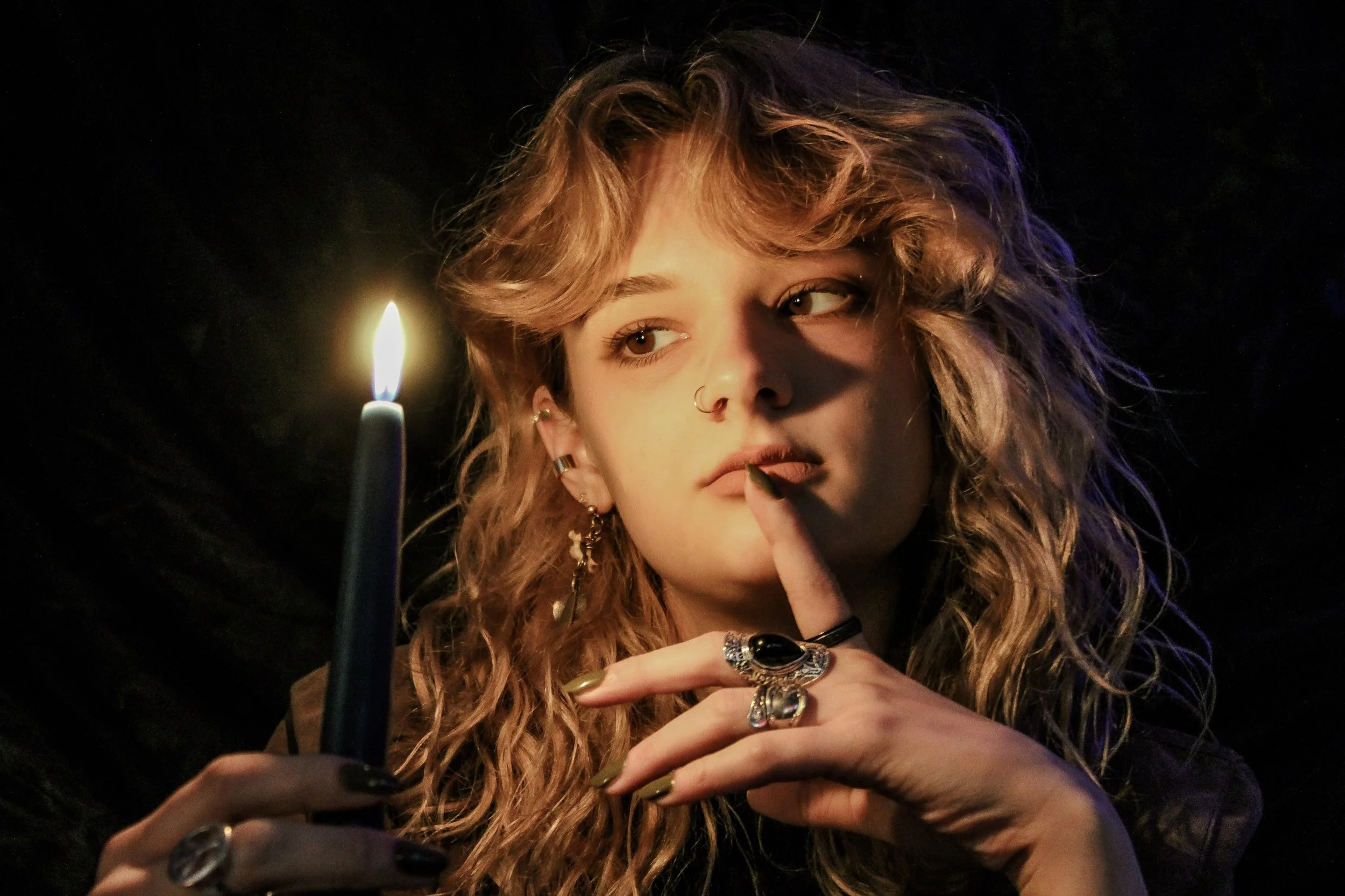 A young woman is holding a lit candle in a dark environment.