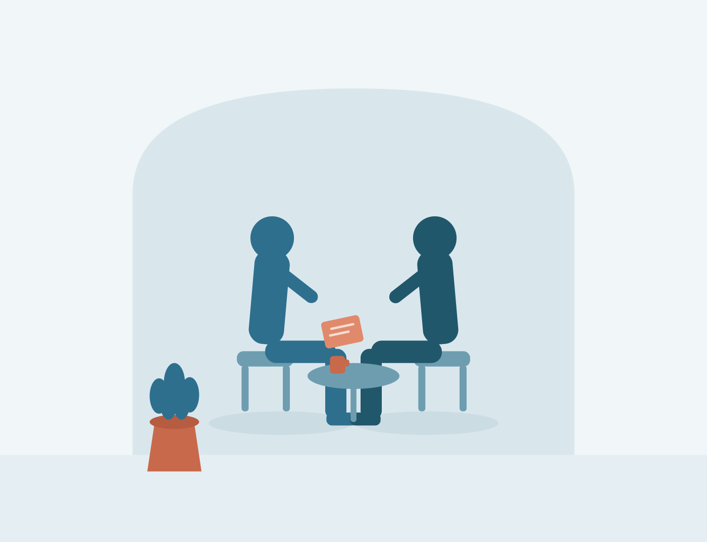 Two people sitting across from each other at a small table, engaging in a conversation, with a potted plant nearby.