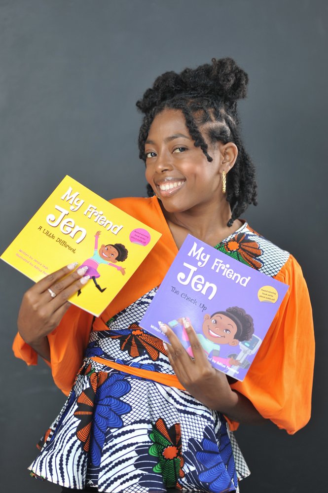 A woman in a colorful dress and orange jacket holding two children's books, smiling at the camera against a gray background.