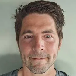Nærbilde av en mann med kort, mørkt hår og skjegg, smilende mot kameraet.