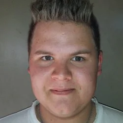 Portrett av en ung mann med lys hud og kort, oppsatt hår, smilende ansikt