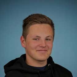 Et portrett av en ung mann med kort, mørk hår og smilende uttrykk, iført en svart hettegenser mot en blå bakgrunn.