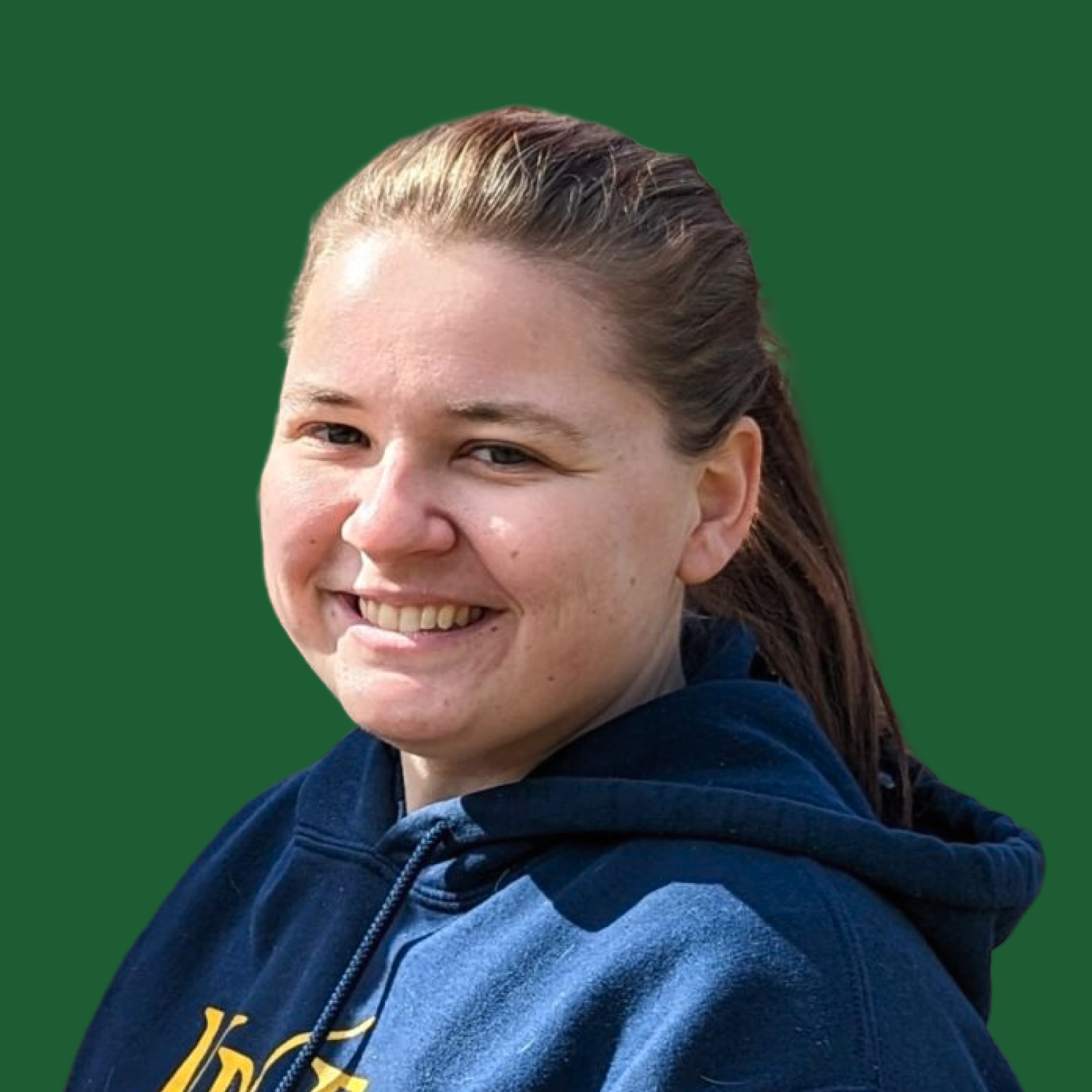 A smiling woman with light skin, brown hair in a ponytail, wearing a navy blue hoodie with yellow text, against a green background.