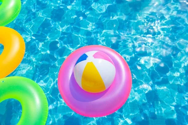 Colorful inflatable pool rings and a beach ball floating in a swimming pool with blue water.