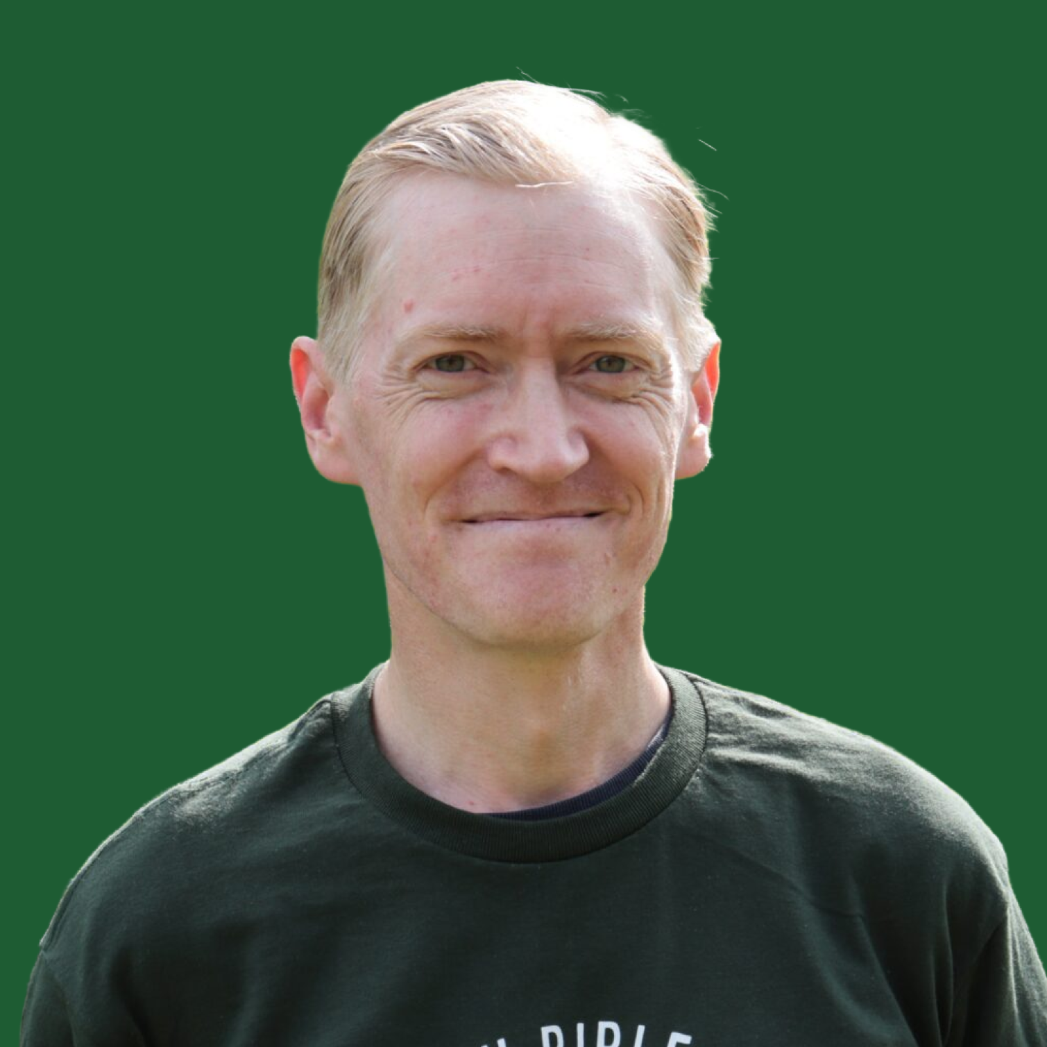 A man with blond hair and light skin, smiling slightly, wearing a dark crewneck shirt against a solid green background.