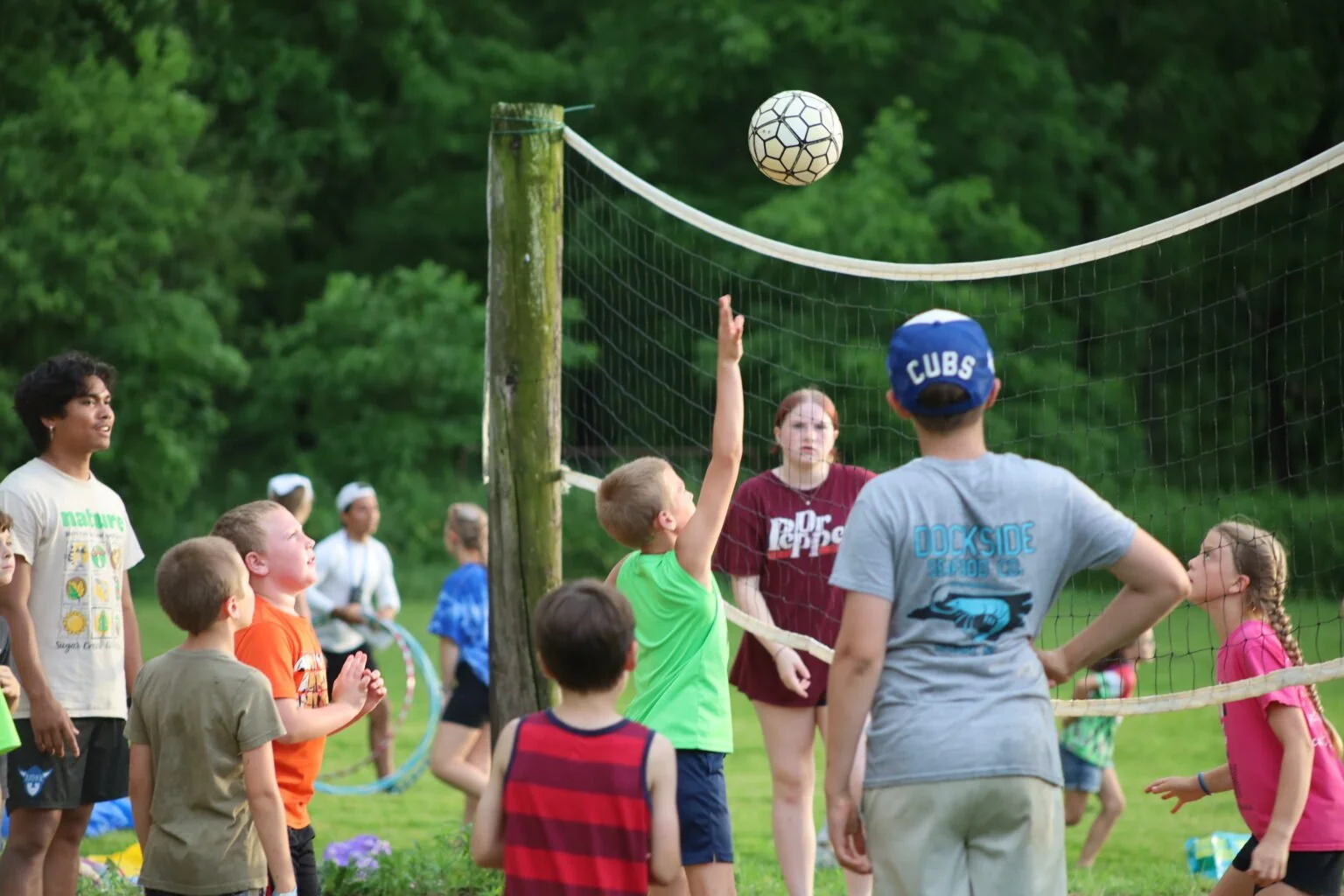 Children playing volleyball outdoors with a green background of trees.