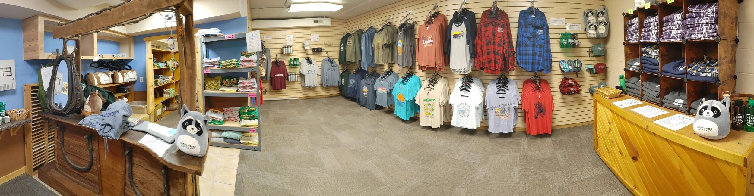 Interior of a retail store with clothing and accessories displayed on shelves and walls, including t-shirts, hoodies, and plush toys.