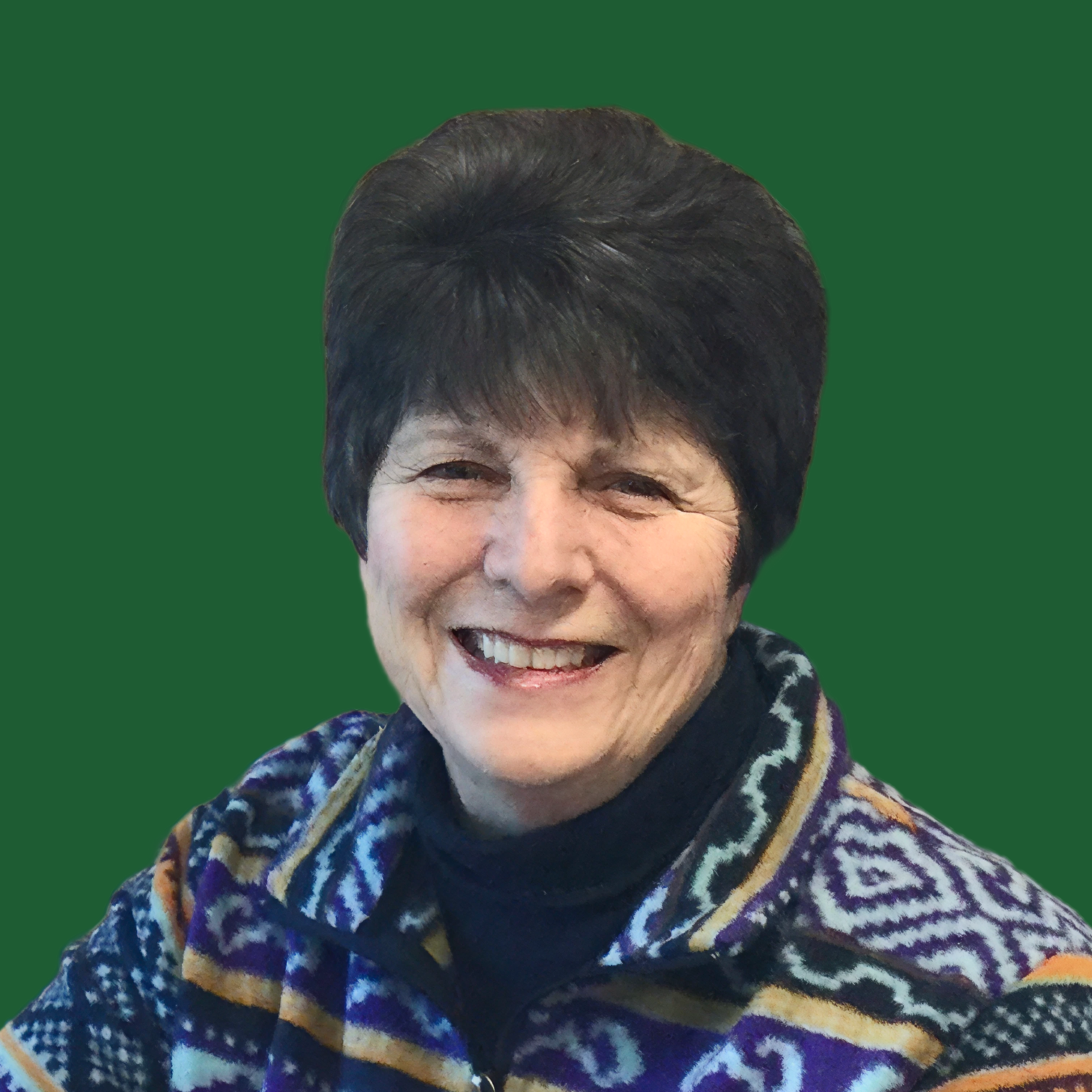 A smiling older woman with short dark hair, wearing a patterned sweater and a scarf, against a solid green background.