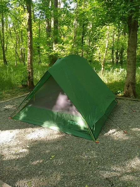 Green camping tent set up in a wooded area with trees and sunlight.