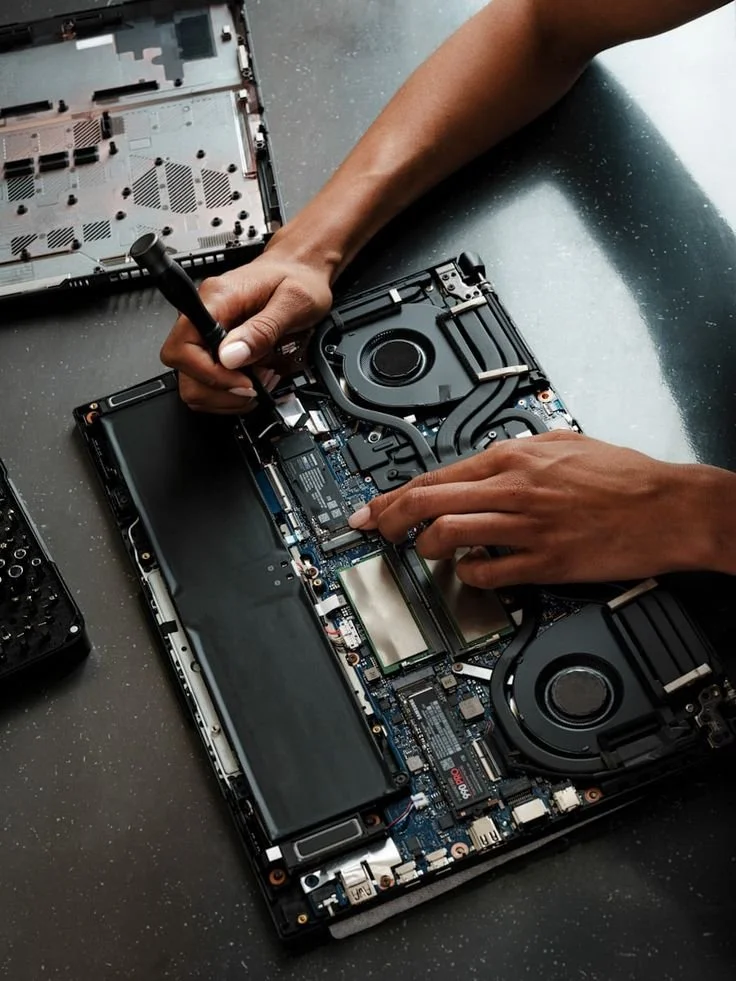 A person repairing a laptop by working inside and handling internal components like the motherboard and cooling system.