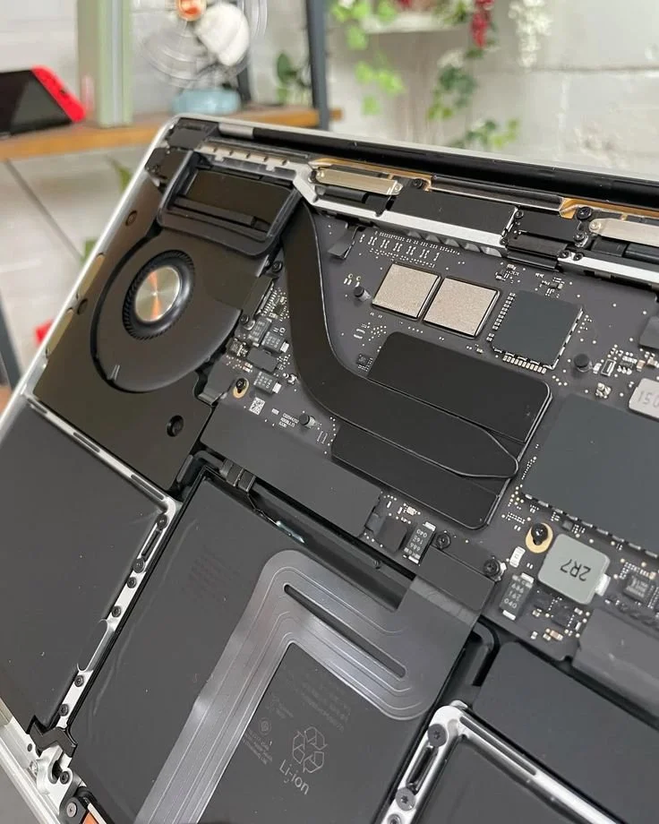 Close-up of an open laptop showing internal components, including a cooling fan, circuit board, and battery.