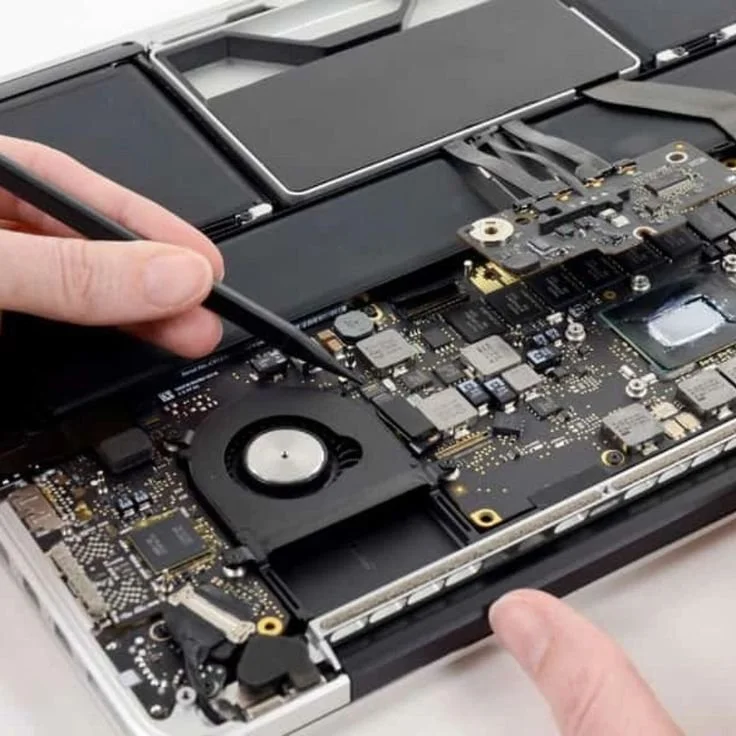 Close-up of a technician's hands repairing a disassembled laptop, using a tool to work on the internal circuit board and components.