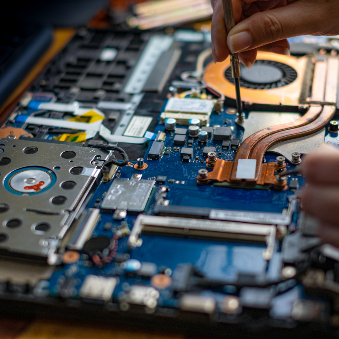 Person repairing a laptop by tightening screws on the internal circuit board with a screwdriver.