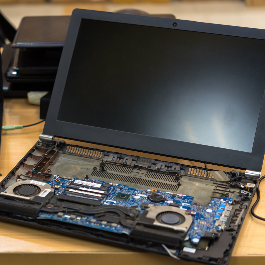 Disassembled laptop with open screen, showing internal components on a wooden table.